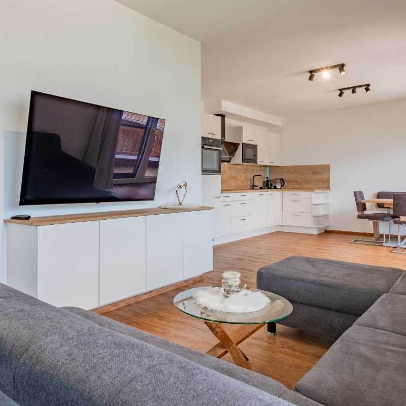 Gemütlicher Wohnraum mit Sofa und Fernseher, offene Küche im Hintergrund der Ferienwohnung Hoferlitzlhubgut in Mittersill.