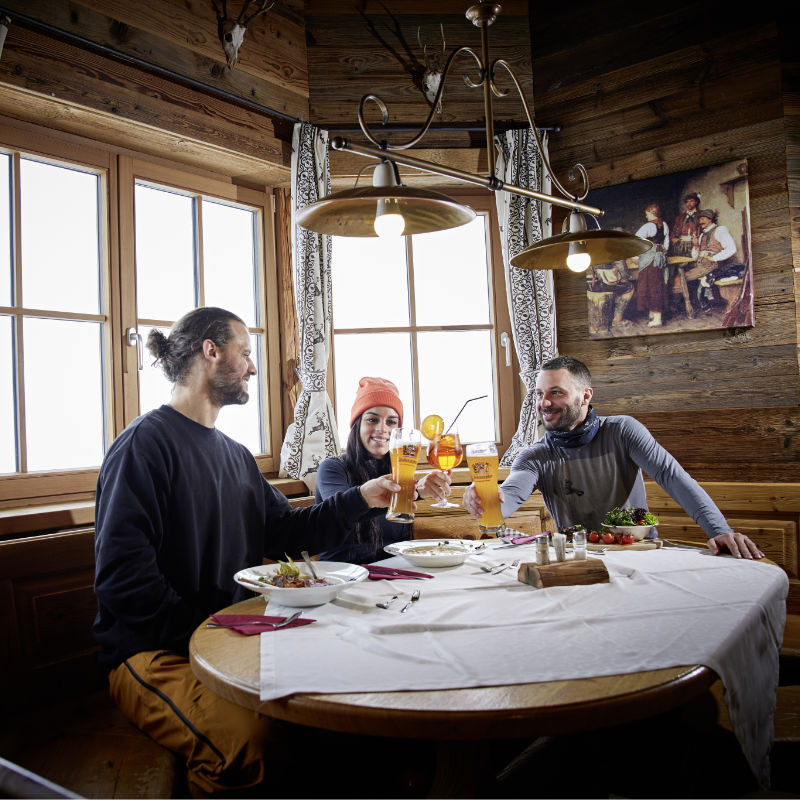 Two men and a woman toasting with drinks in a rustic hut in Mittersill in a cozy atmosphere.