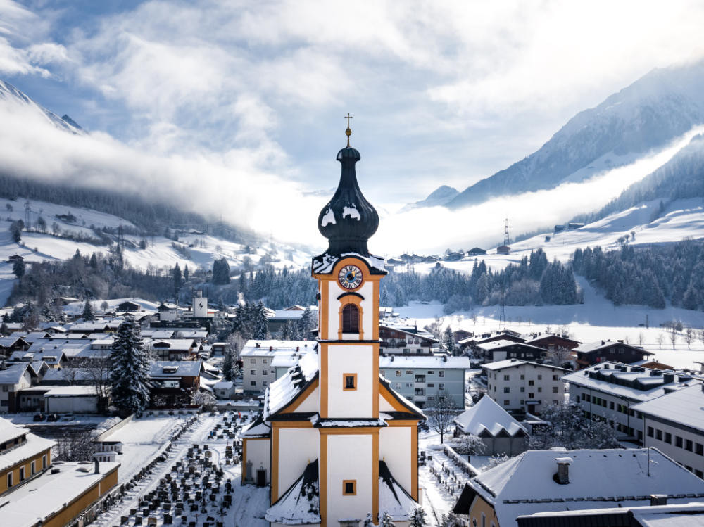 Luftaufnahme von Mittersill mit einer Kirche im Vordergrund, eingebettet in die malerische Landschaft der Alpen.