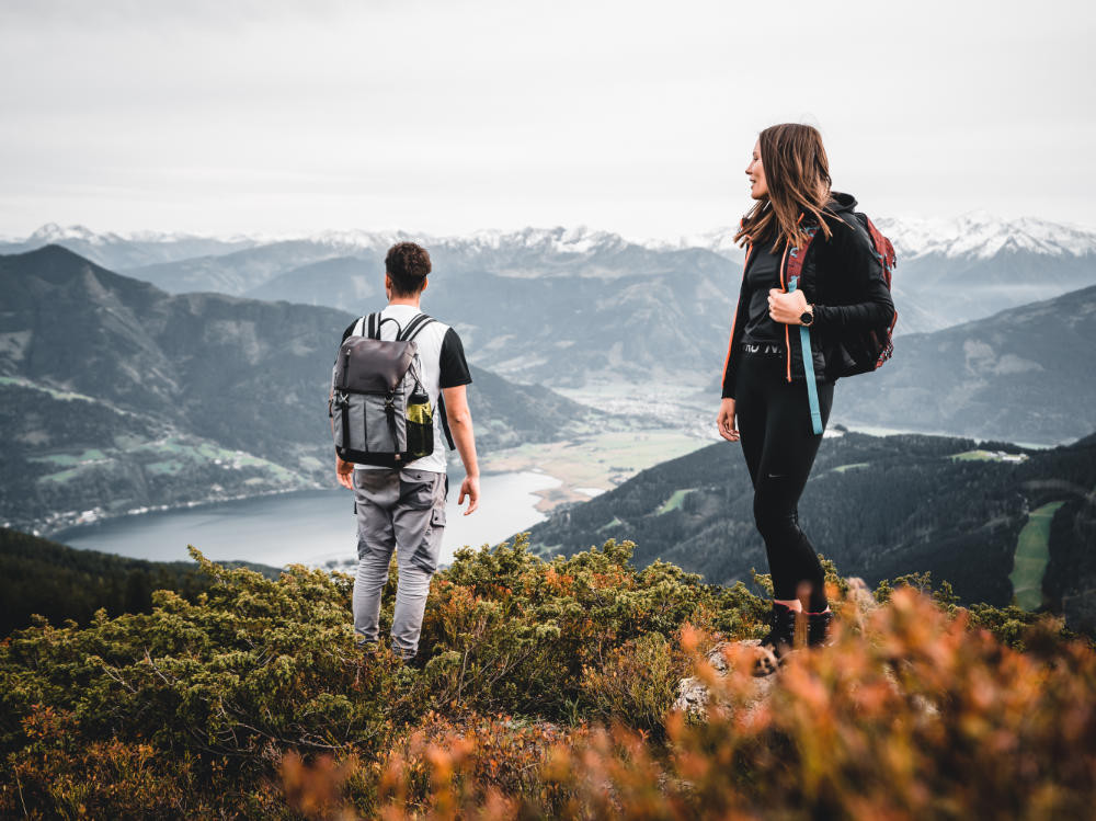 Twee wandelaars staan op de Schmittenhöhe bij Zell am See en kijken uit over het meer van Zell en de omringende bergen.