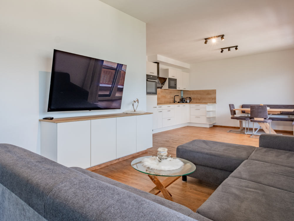 Woonkamer van de vakantiewoning Hoferlitzlhubgut met gezellige bank, grote TV en open keuken op de achtergrond.