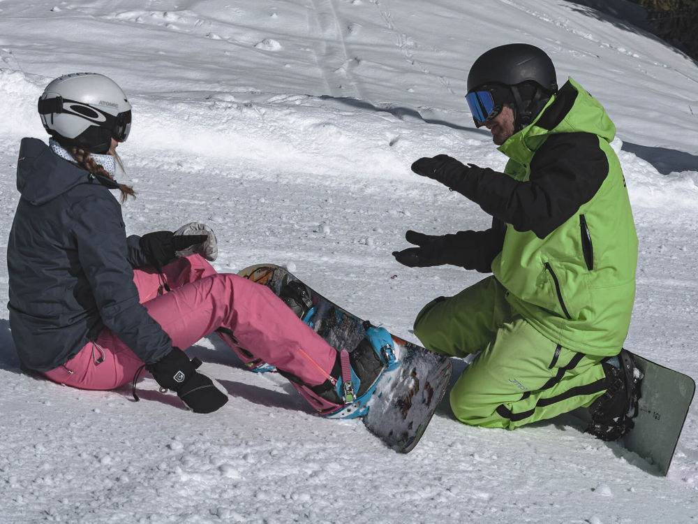 Snowboard instructor explains to a student how to keep her balance on the board during a lesson in the KitzSki ski area.
